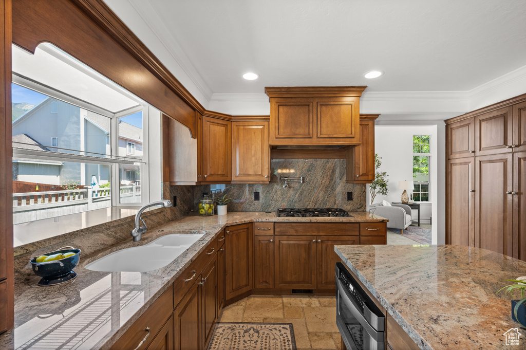 Kitchen with a sink, ornamental molding, gas stovetop, backsplash, and light stone counters