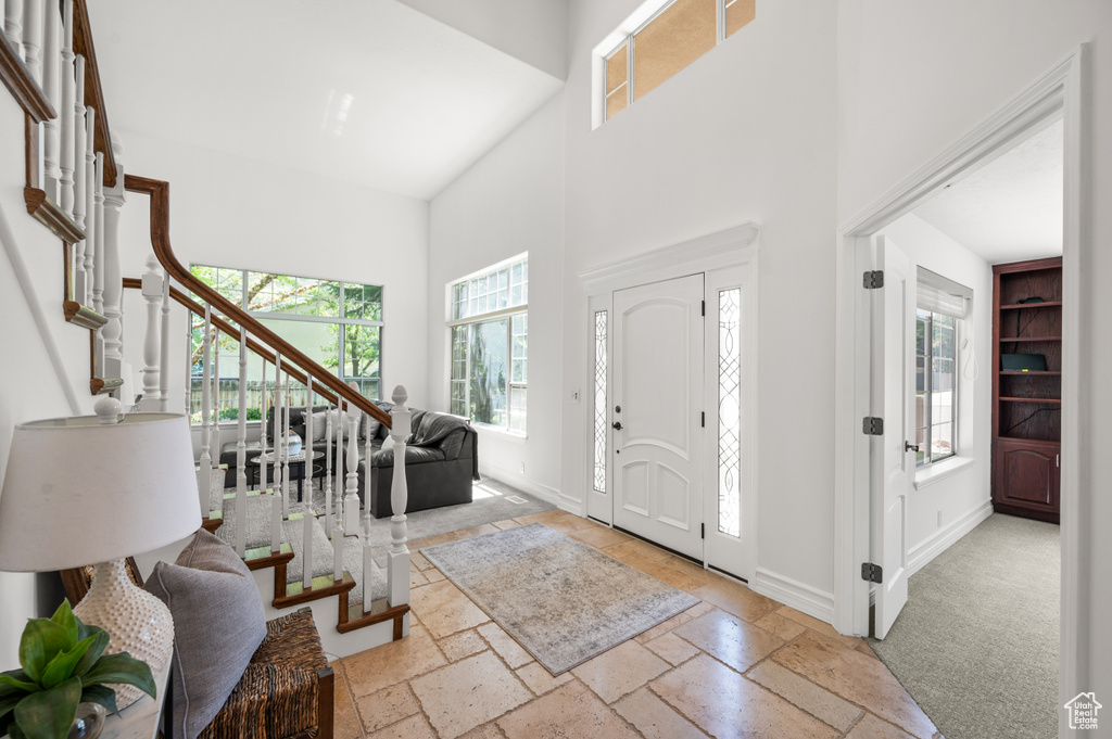 Foyer with stairway, a towering ceiling, baseboards, and stone tile flooring