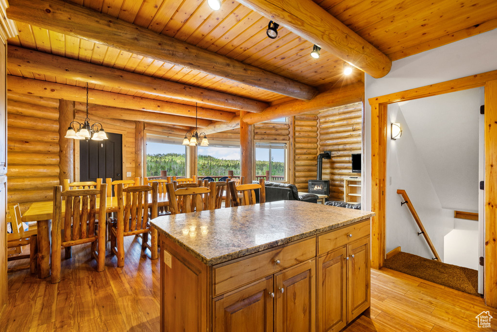 Kitchen with a wood stove, a chandelier, light wood-style flooring, rustic walls, and wooden ceiling with exposed beams