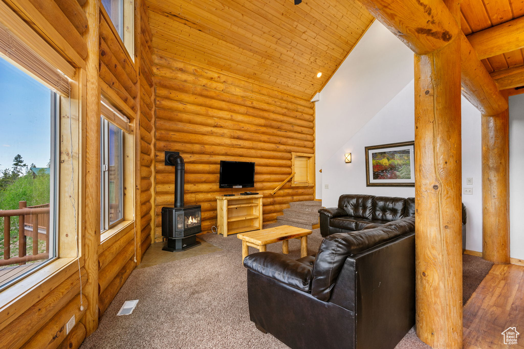 Carpeted living room with high vaulted ceiling, log walls, a wood stove, and wooden ceiling