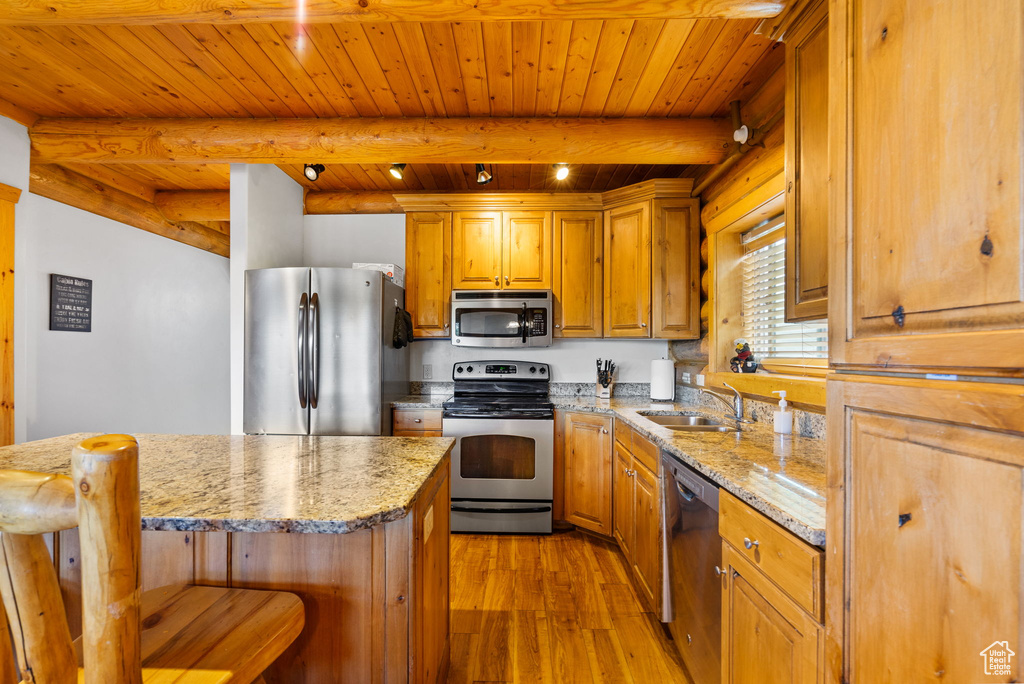 Kitchen featuring stainless steel appliances, a sink, light wood finished floors, a breakfast bar, and light stone countertops