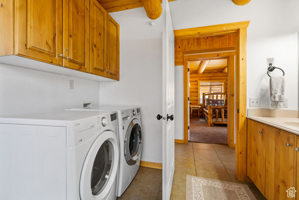 Washroom featuring separate washer and dryer, cabinet space, light tile patterned floors, rustic walls, and baseboards