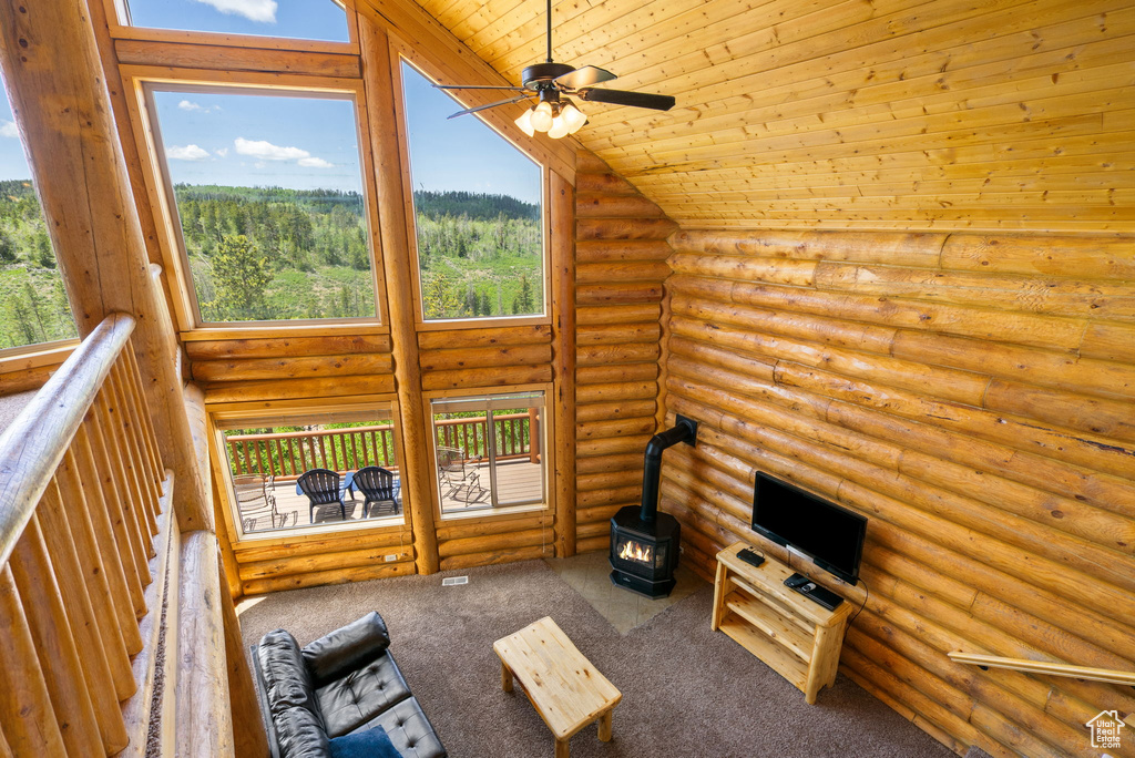 Unfurnished living room with a wood stove, plenty of natural light, a ceiling fan, wooden ceiling, and log walls