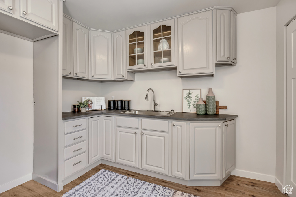 Kitchen featuring a sink, dark countertops, glass insert cabinets, baseboards, and light wood finished floors