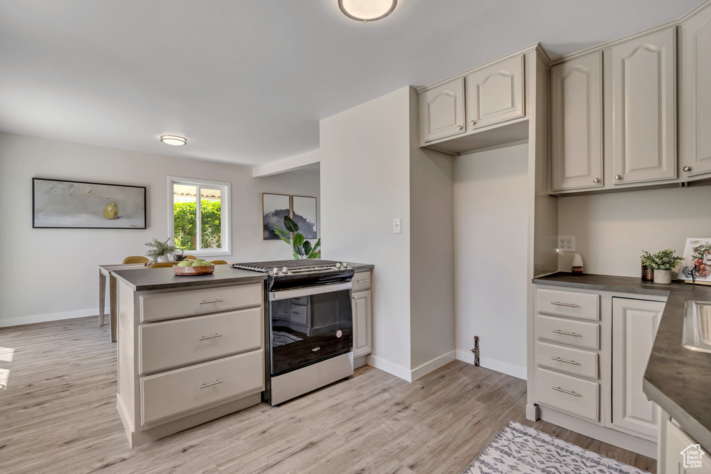 Kitchen featuring stainless steel gas range, dark countertops, light wood-style flooring, and baseboards