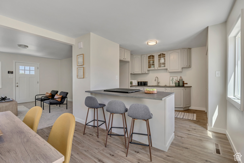 Kitchen featuring a kitchen bar, glass insert cabinets, light wood-type flooring, and a sink