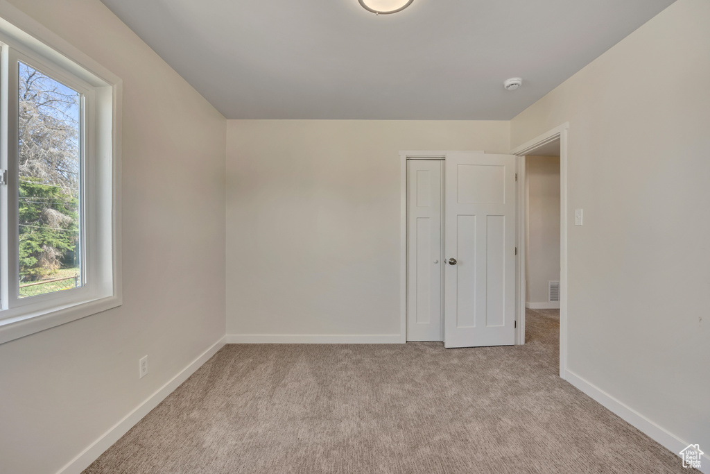 Unfurnished bedroom with multiple windows, light colored carpet, baseboards, and a closet