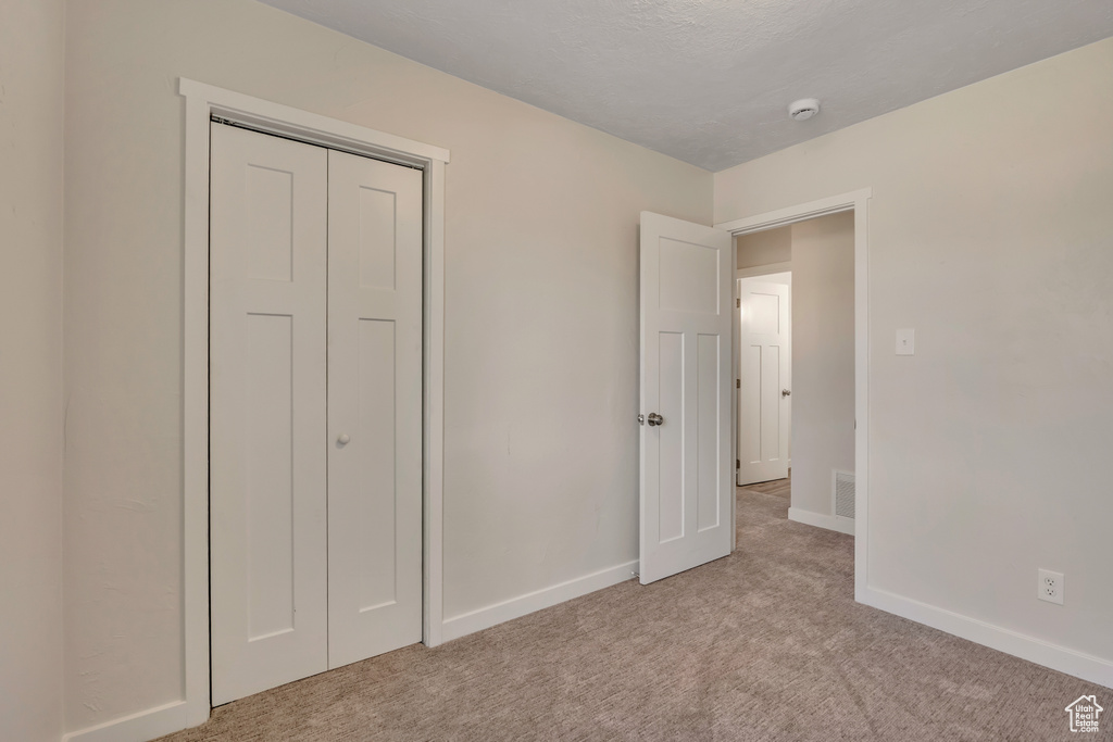 Unfurnished bedroom featuring light colored carpet, baseboards, and a closet