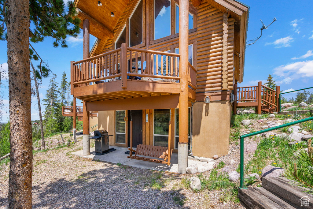 Back of house featuring log exterior, a deck, and a patio