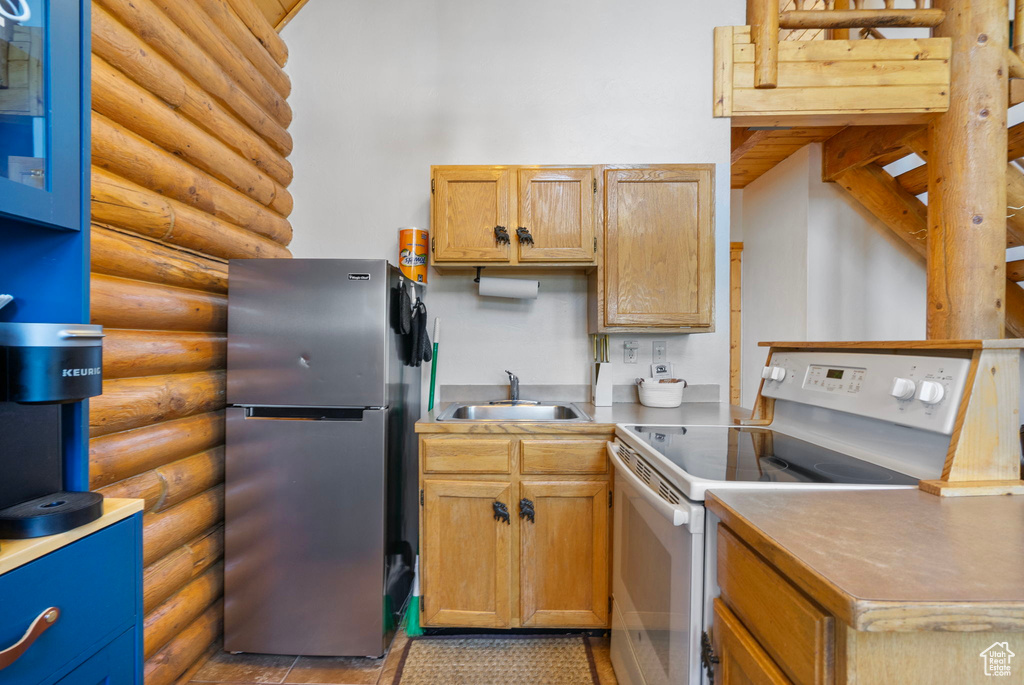 Kitchen with freestanding refrigerator, white range with electric stovetop, log walls, and a sink