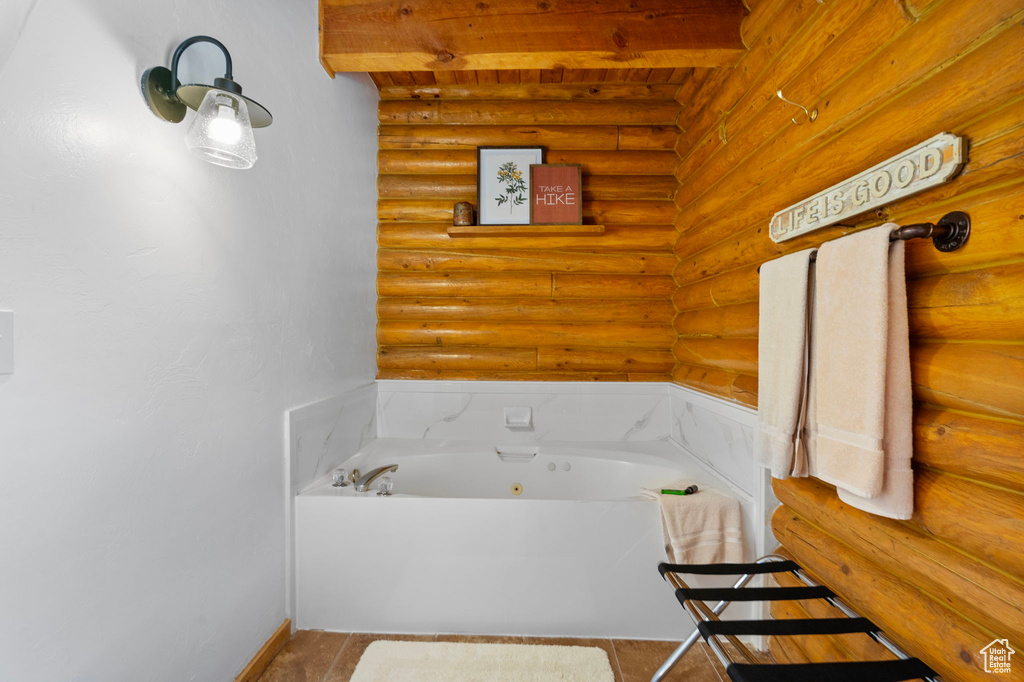 Bathroom with log walls, a tub with jets, beamed ceiling, baseboards, and tile patterned flooring