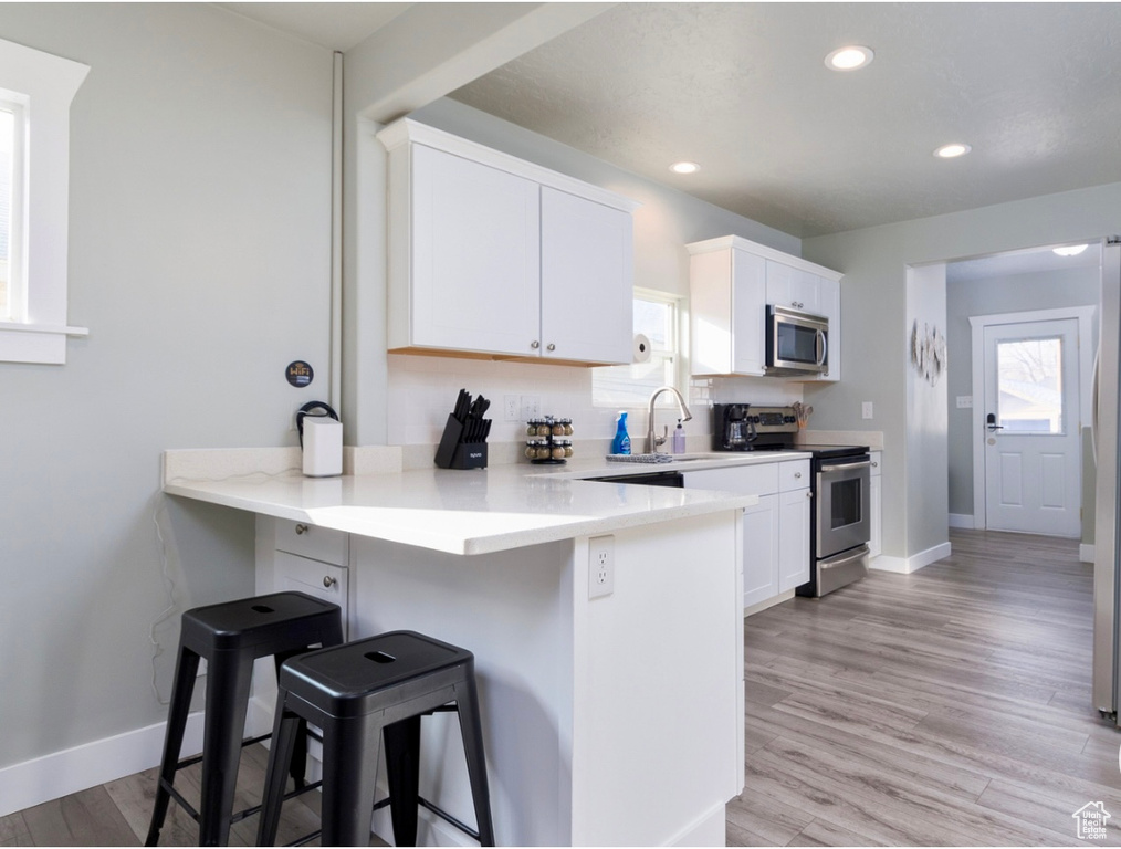Kitchen featuring appliances with stainless steel finishes, a sink, a breakfast bar, white cabinets, and recessed lighting
