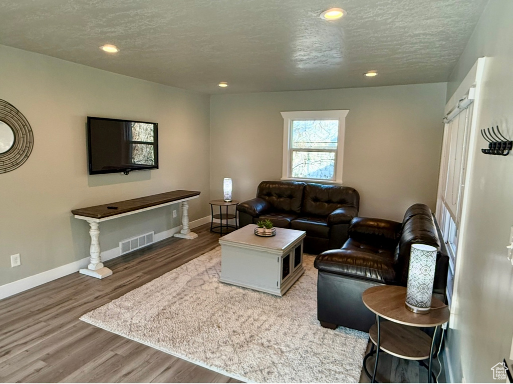 Living room featuring wood finished floors, a textured ceiling, baseboards, and recessed lighting