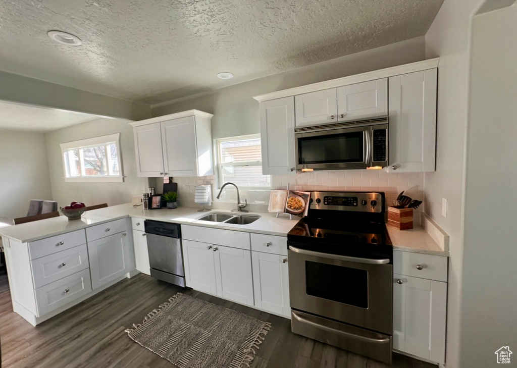 Kitchen with appliances with stainless steel finishes, a sink, a peninsula, light countertops, and a textured ceiling