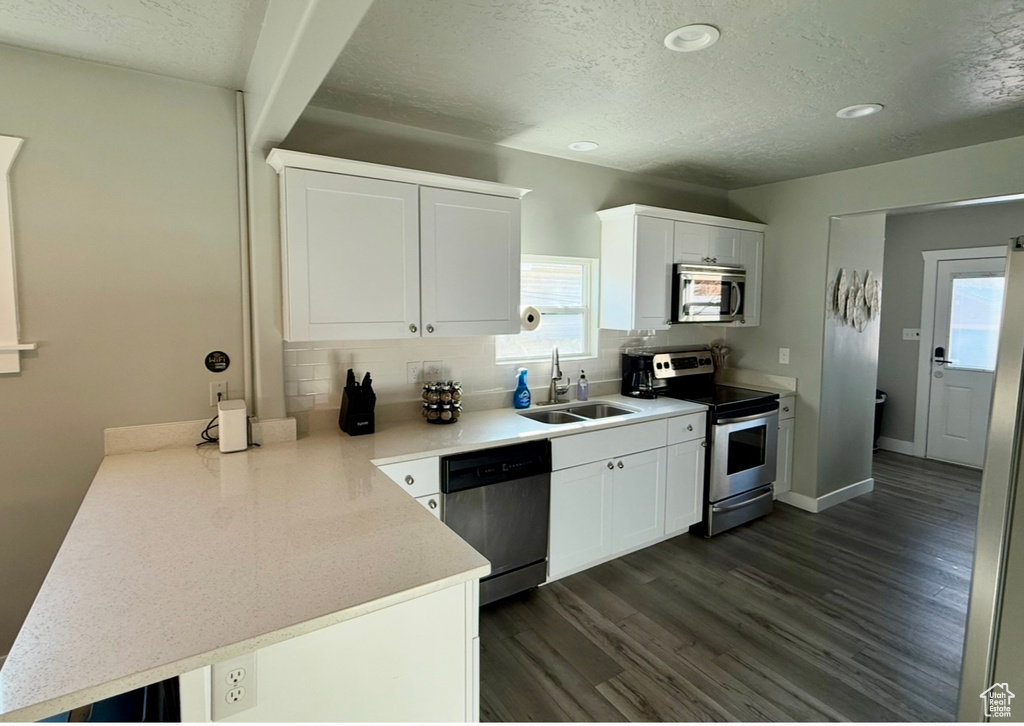 Kitchen featuring stainless steel appliances, a peninsula, a sink, a textured ceiling, and tasteful backsplash