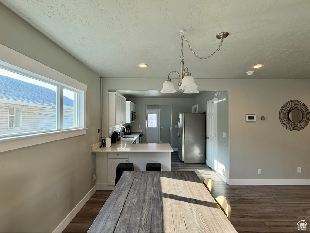 Kitchen featuring stainless steel appliances, a sink, a peninsula, white cabinetry, and light countertops