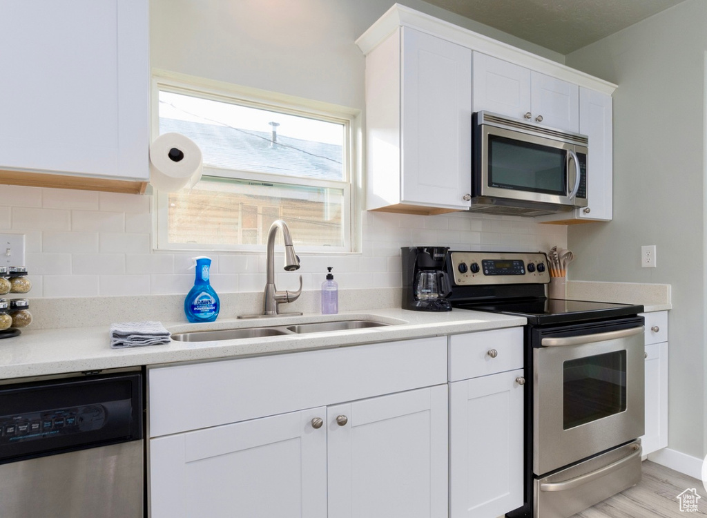 Kitchen with stainless steel appliances, a sink, white cabinetry, and tasteful backsplash