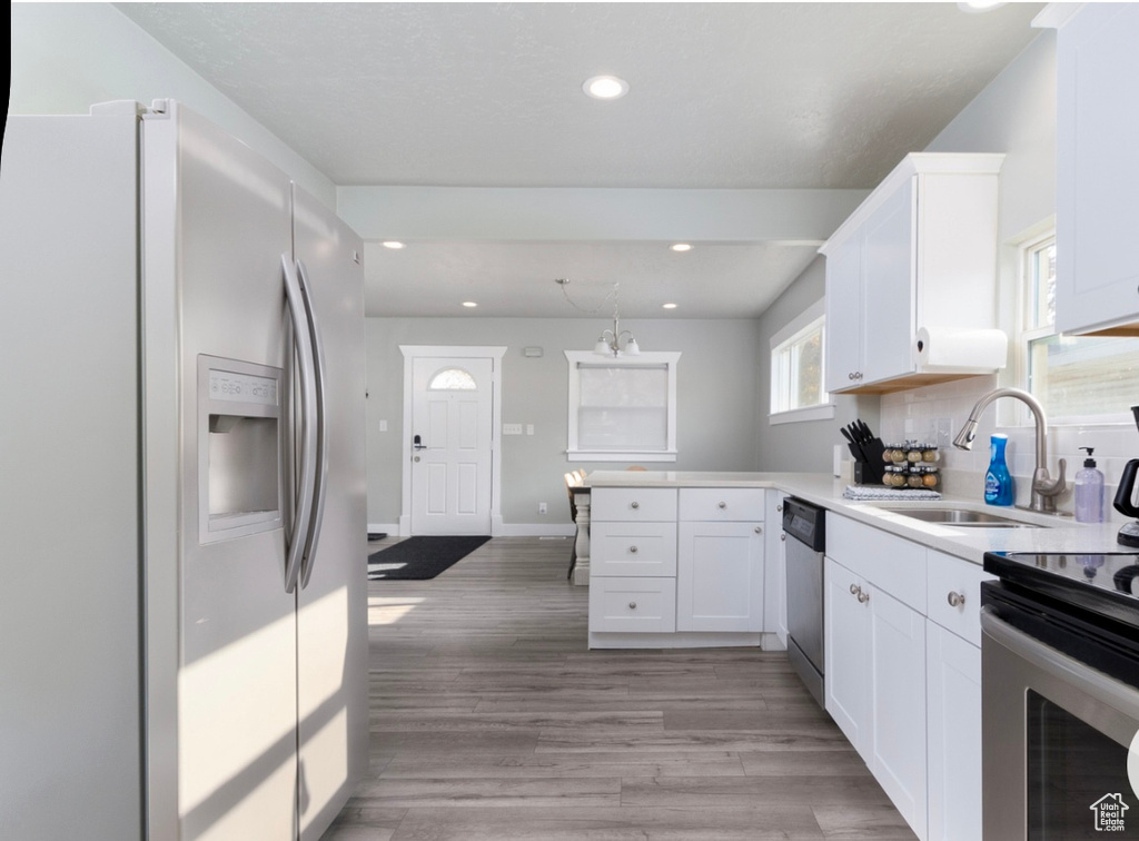 Kitchen featuring appliances with stainless steel finishes, a sink, a peninsula, recessed lighting, and white cabinets