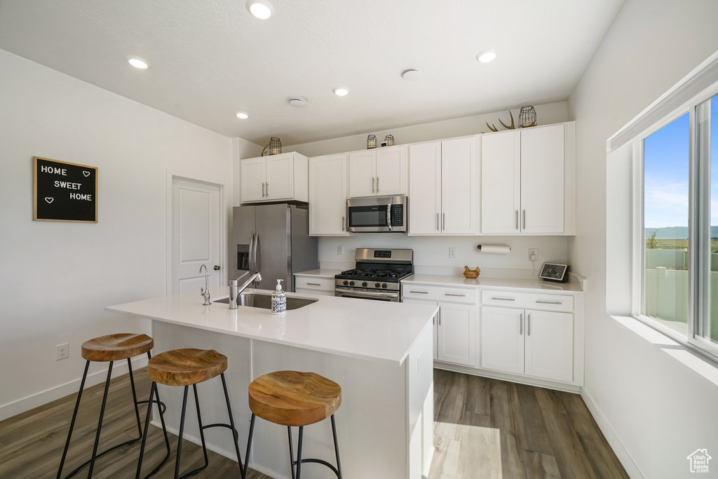 Kitchen with appliances with stainless steel finishes, baseboards, dark wood-style flooring, an island with sink, and a sink