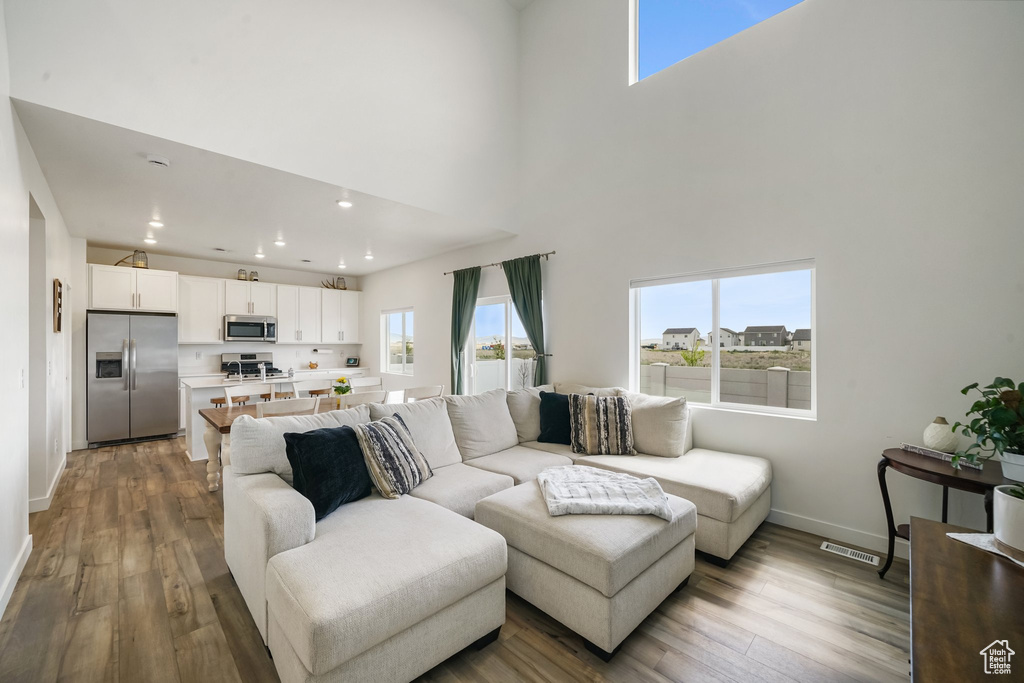 Living area with wood finished floors, baseboards, a towering ceiling, and recessed lighting