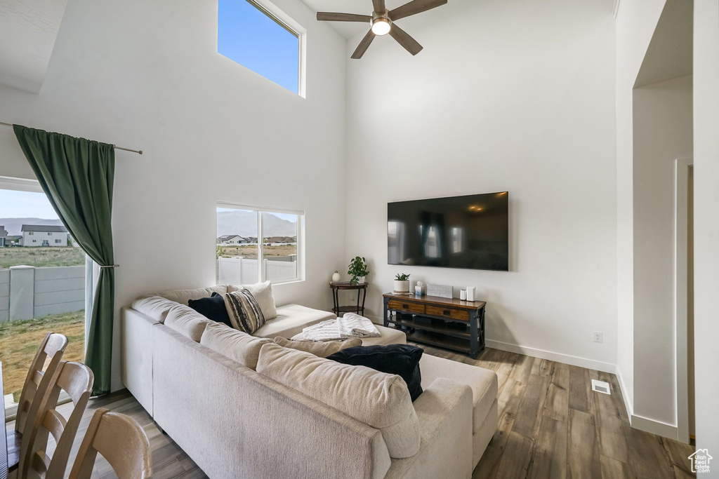Living room with ceiling fan, a high ceiling, wood finished floors, healthy amount of natural light, and baseboards
