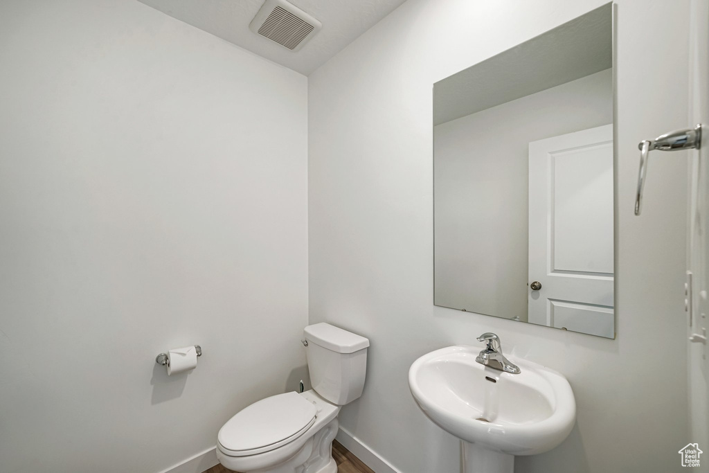 Half bathroom featuring a sink, toilet, baseboards, and wood finished floors