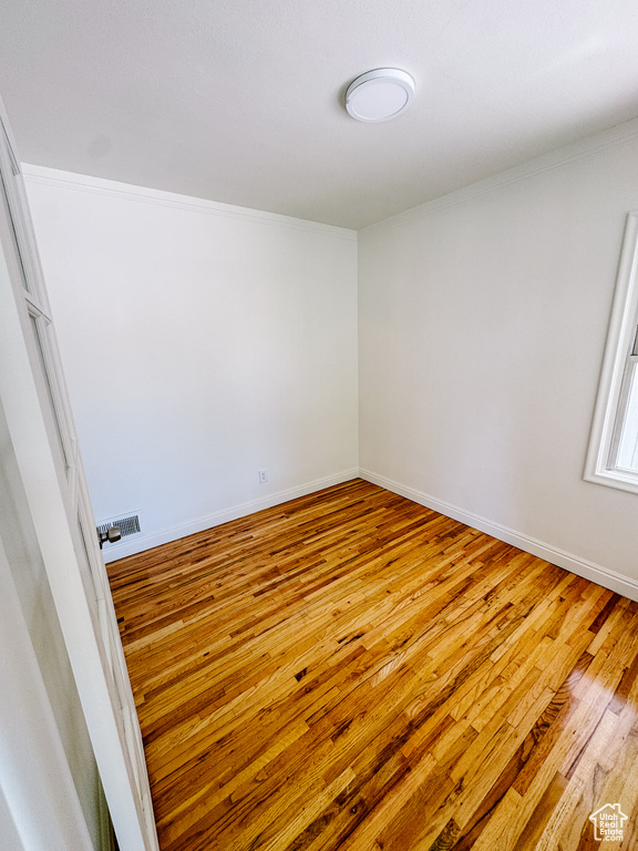 Empty room featuring hardwood / wood-style floors, baseboards, and crown molding