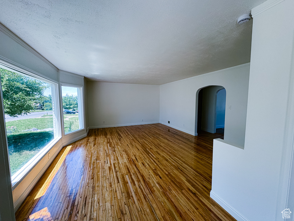 Spare room featuring arched walkways, hardwood / wood-style floors, a smoke detector, baseboards, and a textured ceiling
