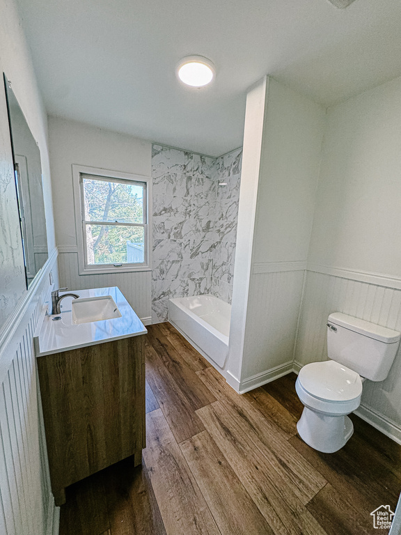 Bathroom with toilet, double vanity, wood finished floors, and wainscoting