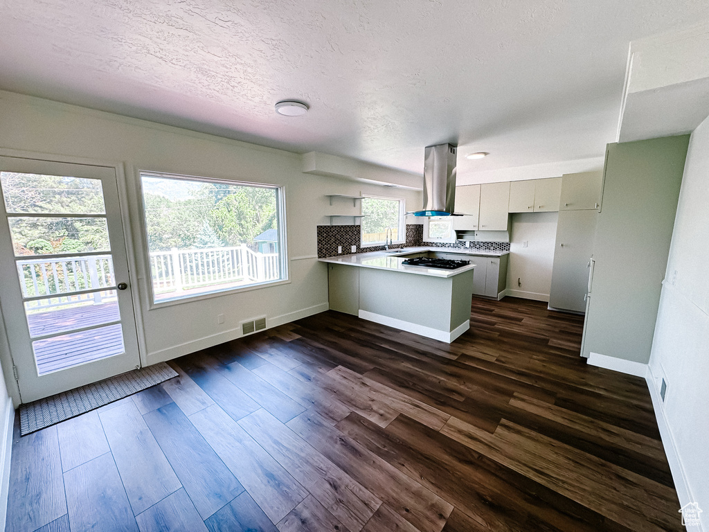 Kitchen featuring island range hood, a peninsula, gas cooktop, dark wood-style flooring, and baseboards