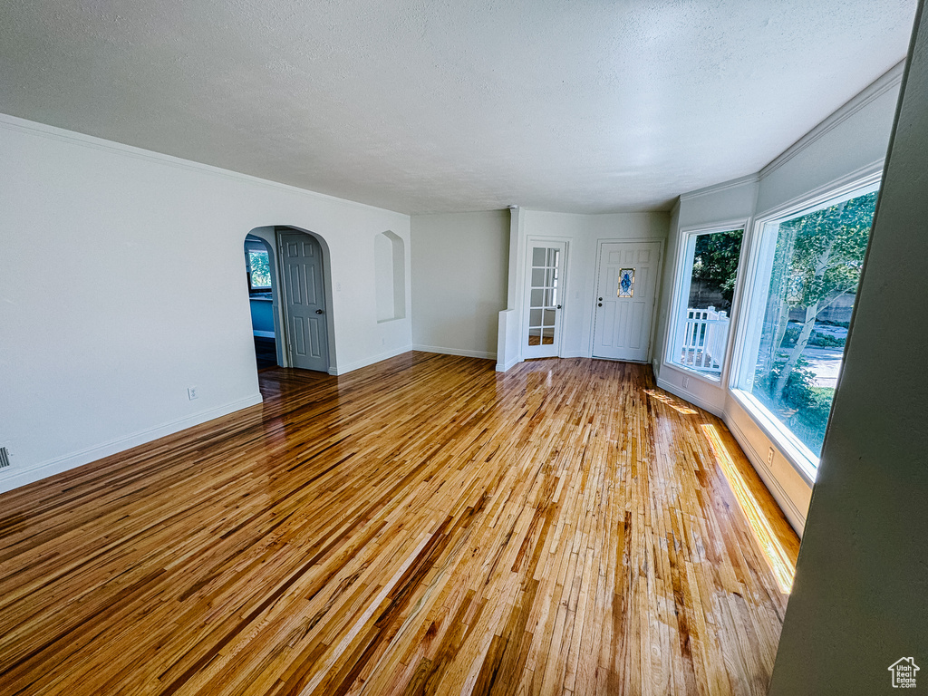 Spare room featuring arched walkways, hardwood / wood-style floors, baseboards, a textured ceiling, and ornamental molding