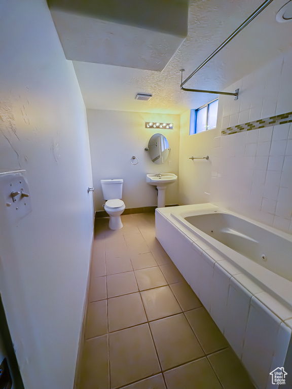 Bathroom featuring toilet, tile patterned floors, a combined bath / shower with jetted tub, baseboards, and a textured ceiling