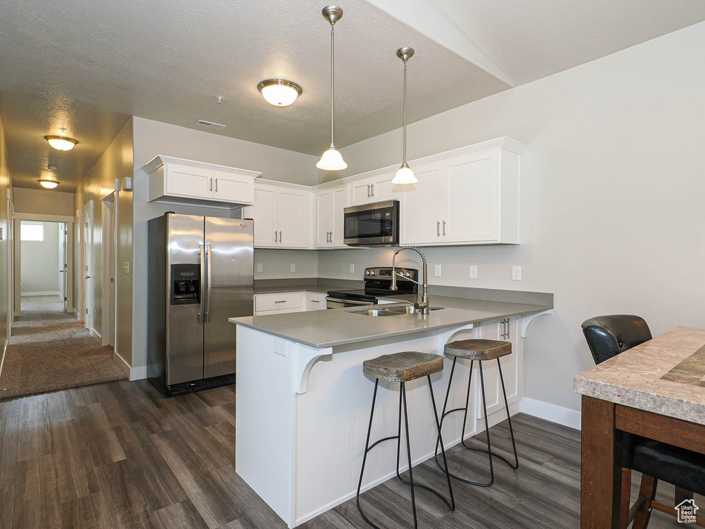 Kitchen featuring stainless steel appliances, a sink, dark wood finished floors, a peninsula, and baseboards