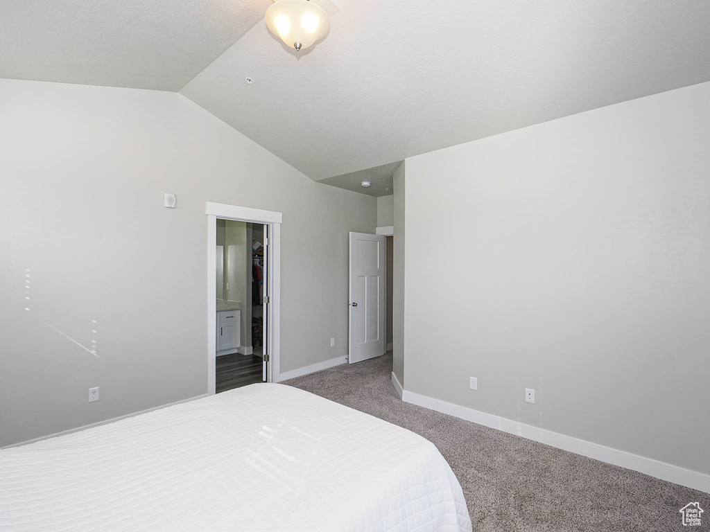 Bedroom with carpet flooring, lofted ceiling, baseboards, and ensuite bathroom
