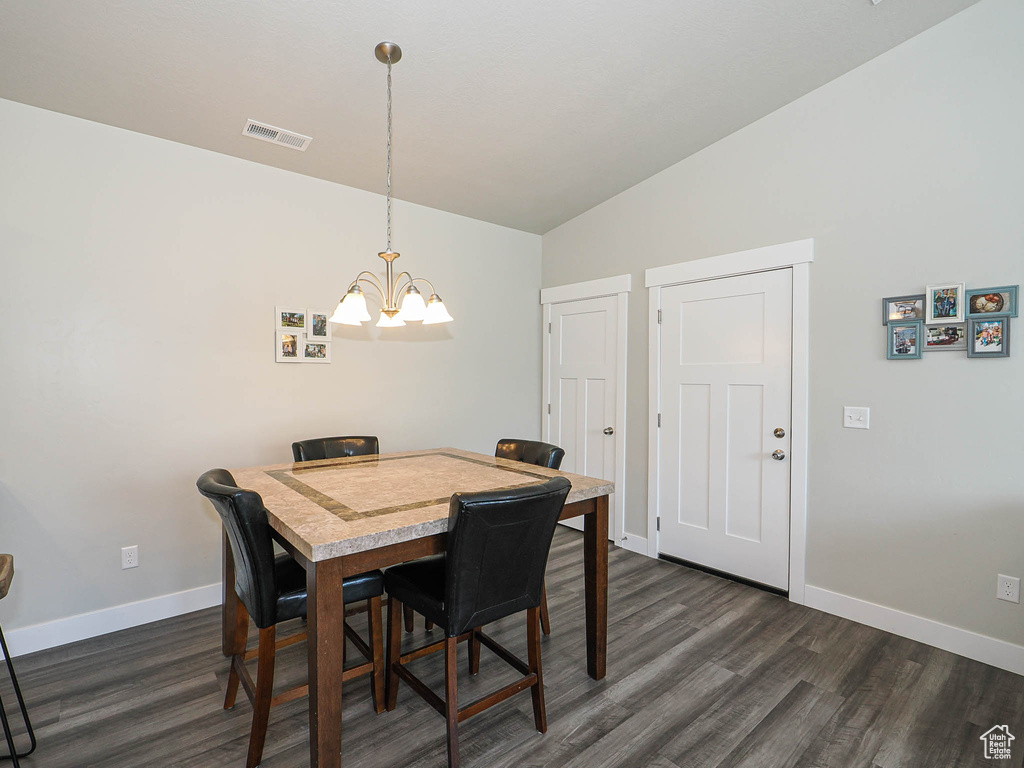 Dining area with vaulted ceiling, a chandelier, dark wood finished floors, and baseboards