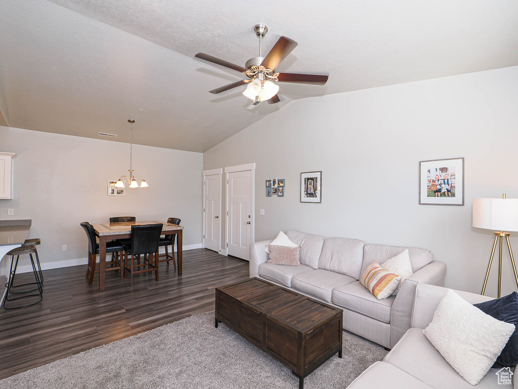 Living room with dark wood-style flooring, vaulted ceiling, a ceiling fan, a chandelier, and baseboards