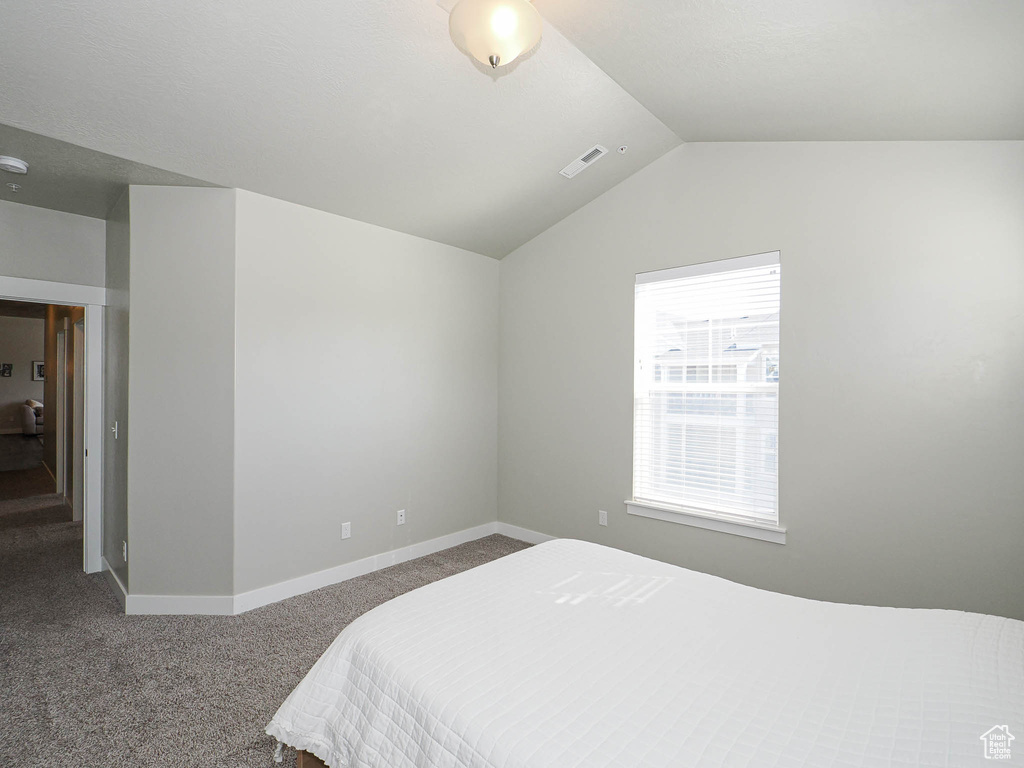 Carpeted bedroom with vaulted ceiling and baseboards
