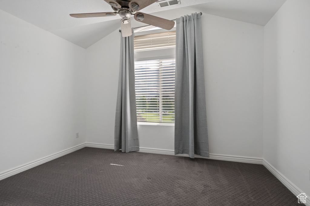 Unfurnished room featuring carpet flooring, ceiling fan, vaulted ceiling, and baseboards