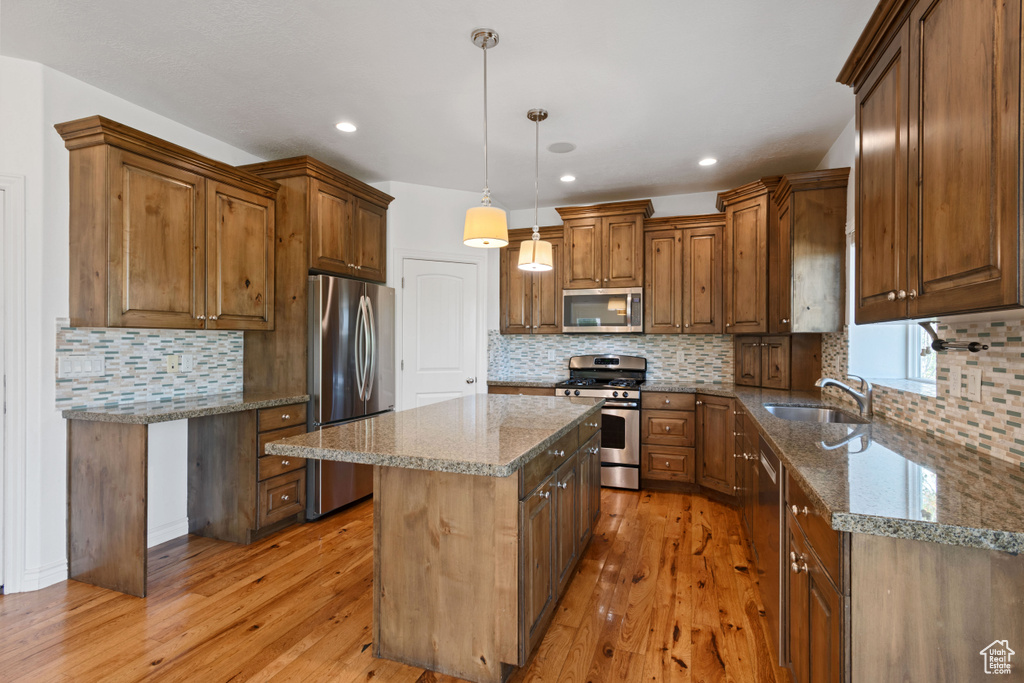 Kitchen with stainless steel appliances, a sink, light wood finished floors, a center island, and recessed lighting
