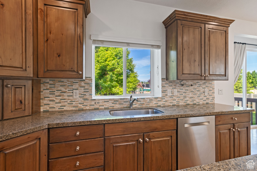 Kitchen featuring dishwasher, a sink, backsplash, brown cabinets, and dark stone countertops