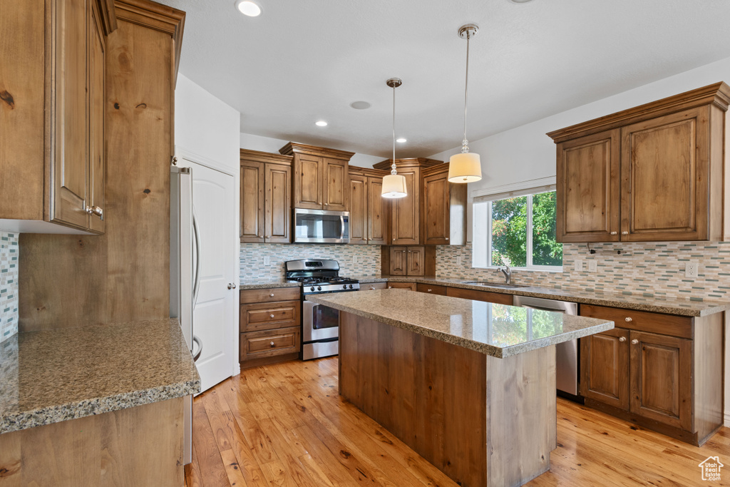 Kitchen with stainless steel appliances, a sink, light wood-style floors, brown cabinetry, and a center island