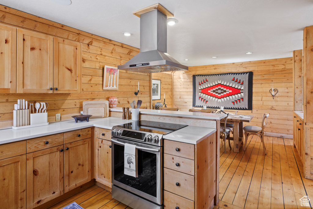 Kitchen with island range hood, stainless steel electric range, a peninsula, wood walls, and light wood-type flooring