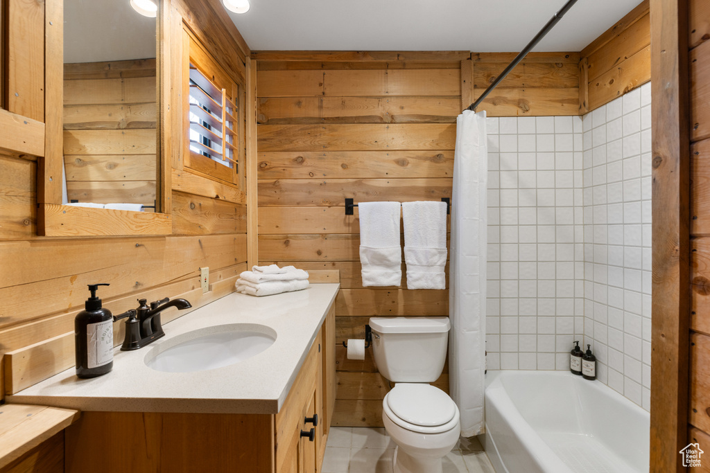Full bathroom with toilet, vanity, wooden walls, and shower / bath combo