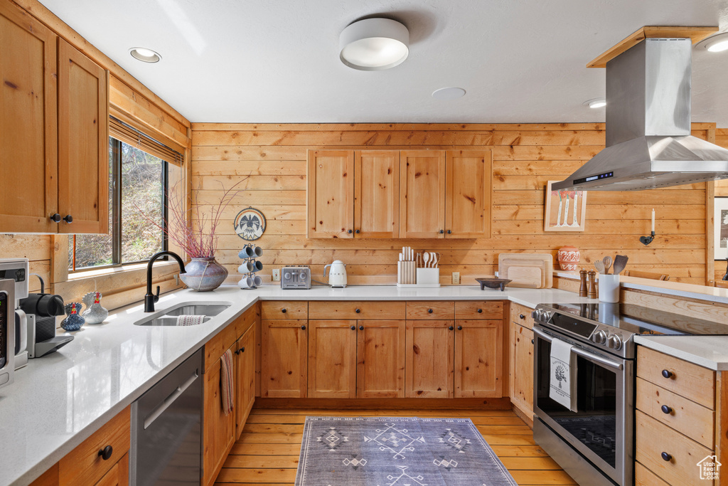 Kitchen with island range hood, a sink, stainless steel appliances, light countertops, and light wood-type flooring