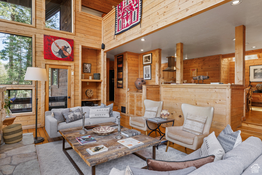 Living area with wooden walls, a high ceiling, wood finished floors, and recessed lighting