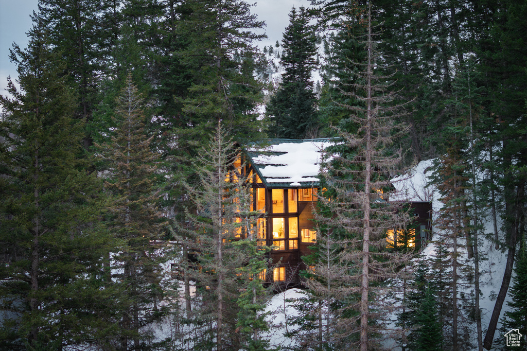 View of snow covered exterior featuring a sunroom and a wooded view