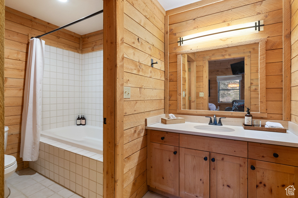 Bathroom with toilet, wooden walls, vanity, tile patterned flooring, and tiled shower / bath