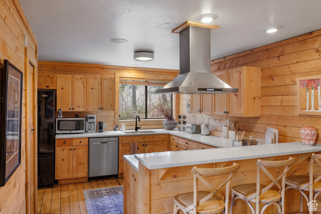 Kitchen with stainless steel appliances, island range hood, a peninsula, a sink, and light brown cabinetry