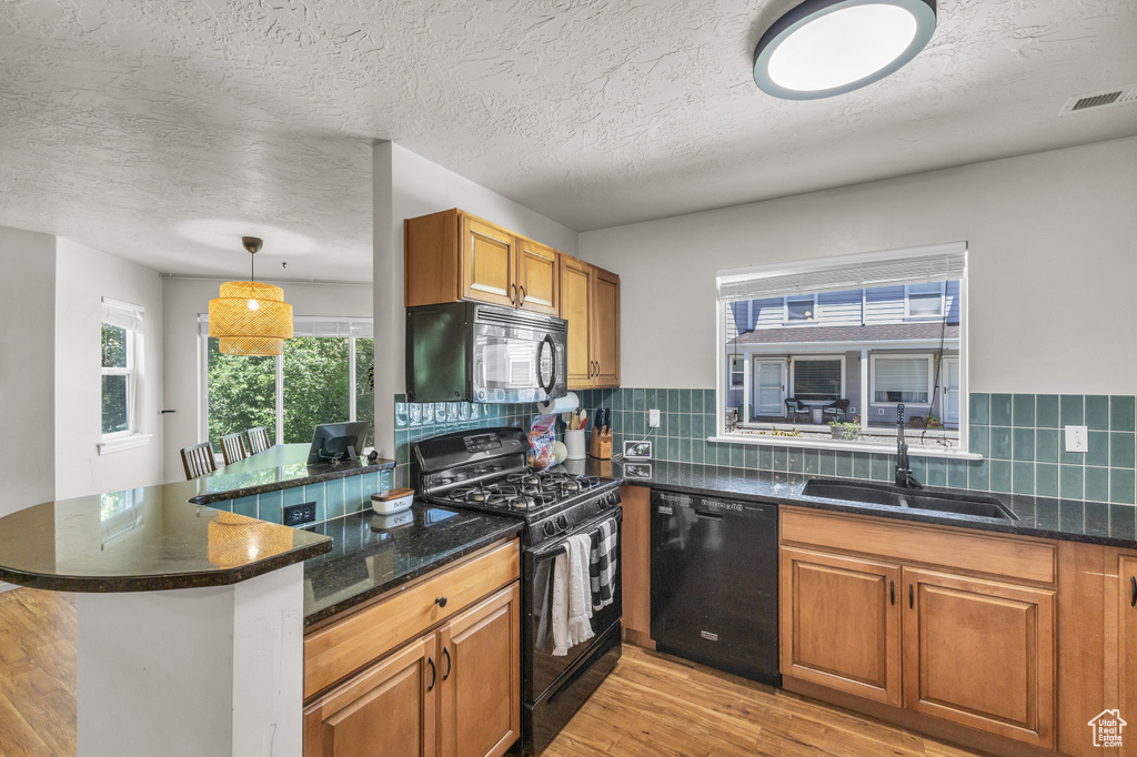 Kitchen with black appliances, a sink, light wood-style floors, brown cabinets, and a peninsula