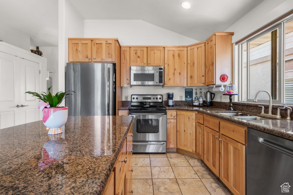 Kitchen featuring appliances with stainless steel finishes, a sink, vaulted ceiling, light marble finish floors, and dark stone countertops